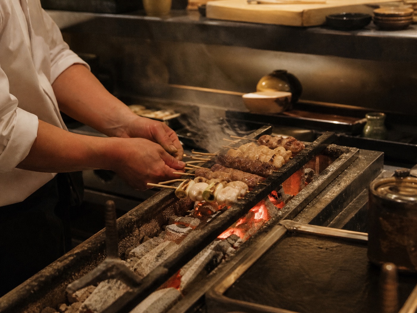 煙が立つ備長炭の焼き場で複数の串を焼く職人